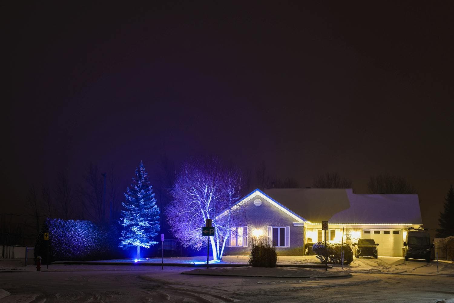 Single-story ranch home at night with warm-white roofline lights along the eaves, snowy yard, and an attached garage extending the horizontal silhouette