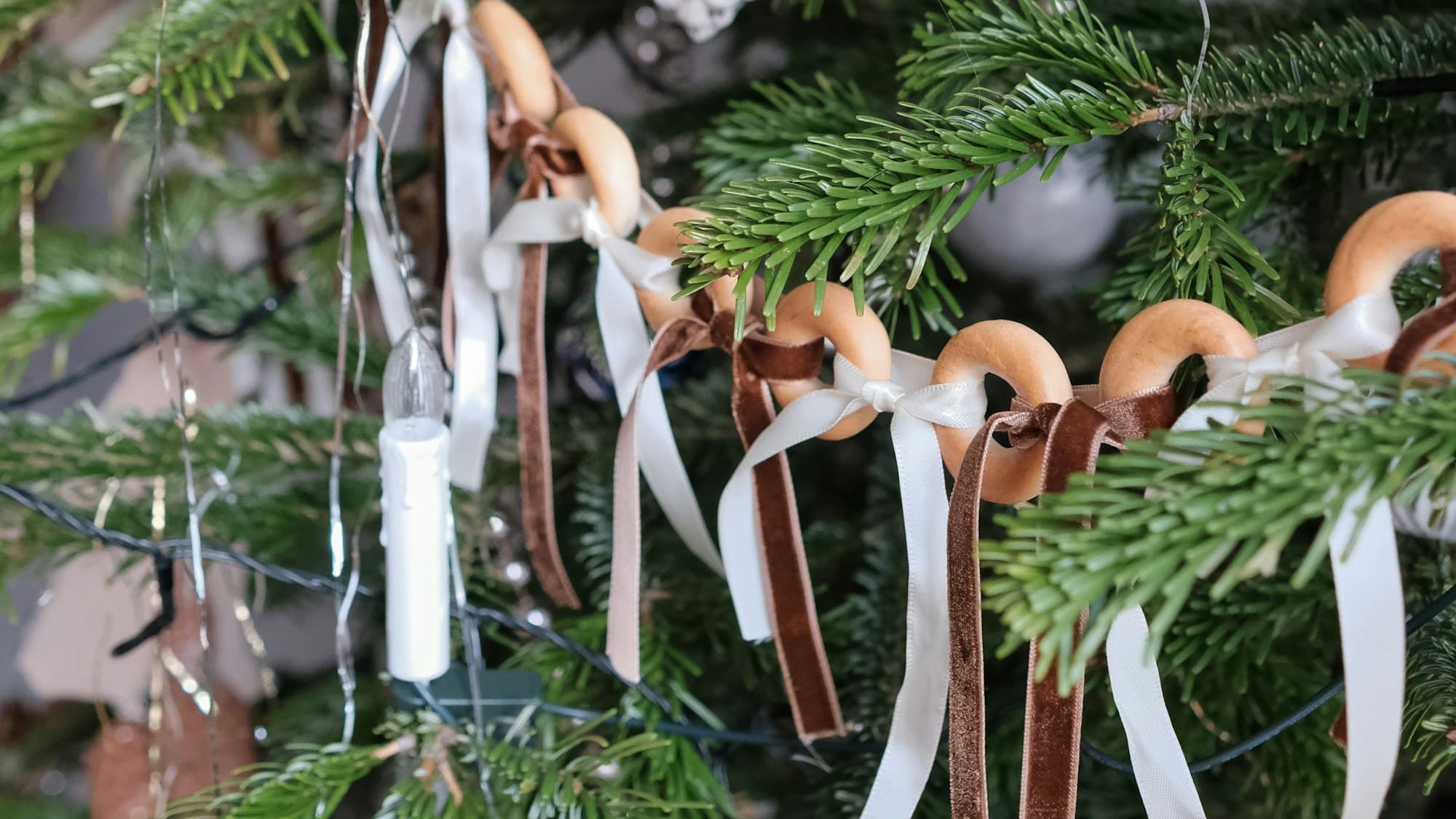 A Christmas tree decorated with handmade natural ornaments — dried orange slices, pinecones, and warm lights — in candlelight