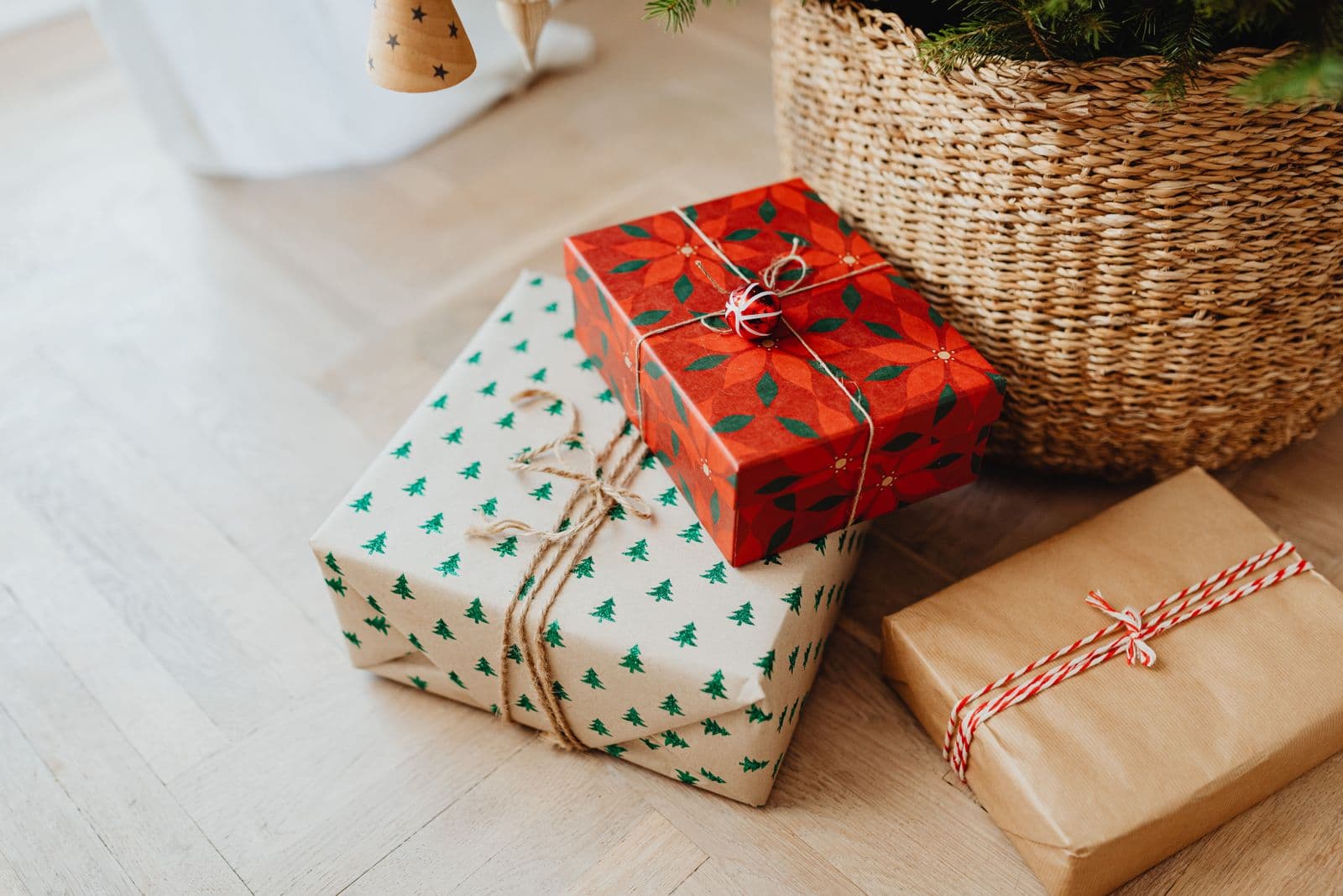 Christmas gifts wrapped in festive paper with ribbon lying beneath a lit Christmas tree