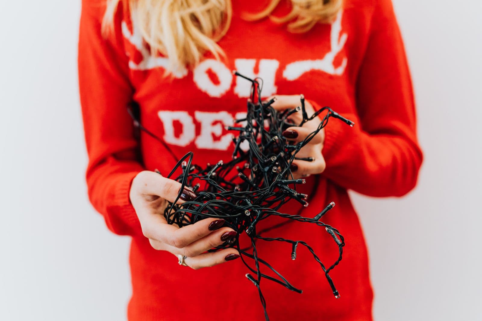 A person in a red Christmas sweater holding a tangled bundle of dark-wire string lights in both hands